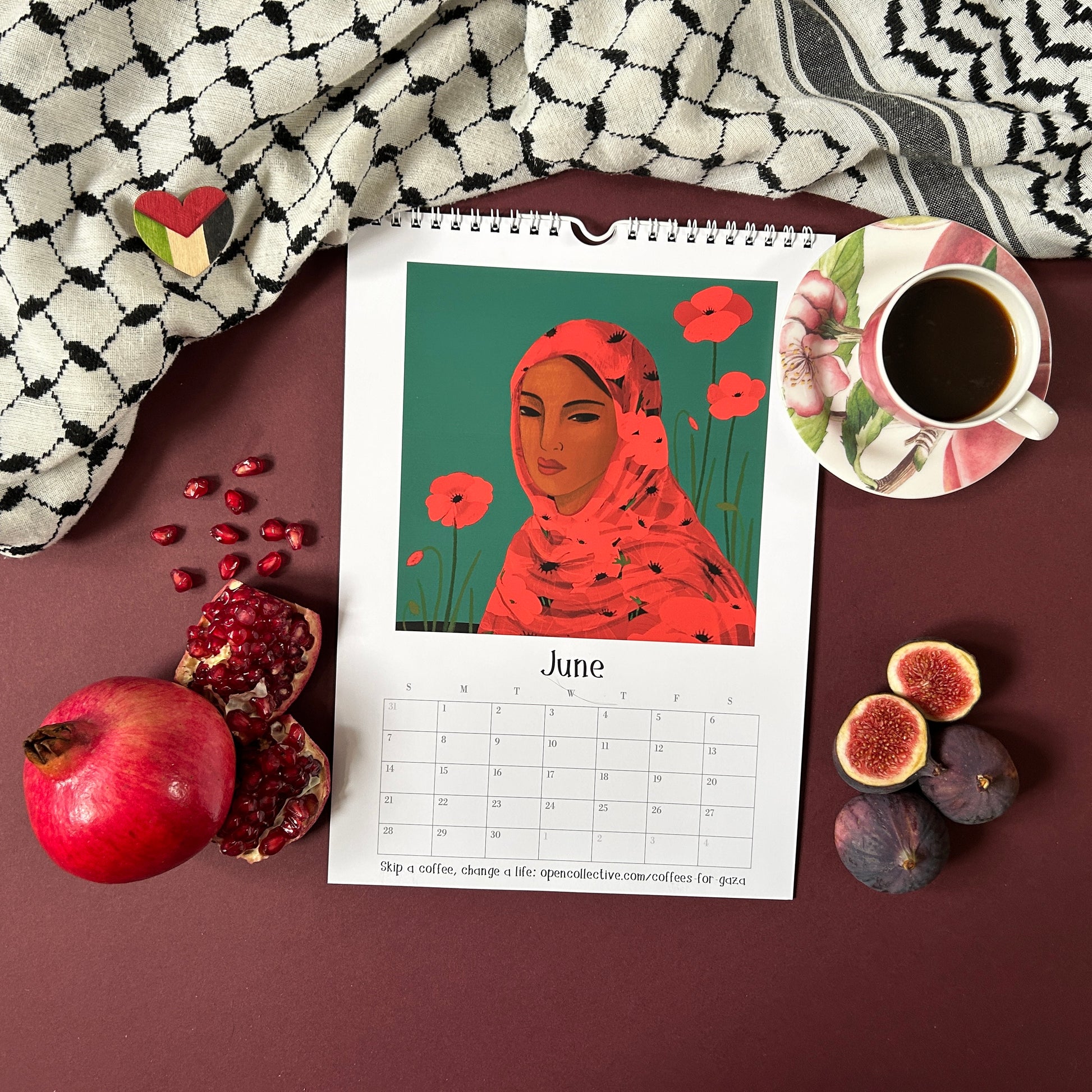 Calendar for June with a Palestinian woman's portrait, surrounded by pomegranate, figs, and a cup of coffee with a keffiyeh.