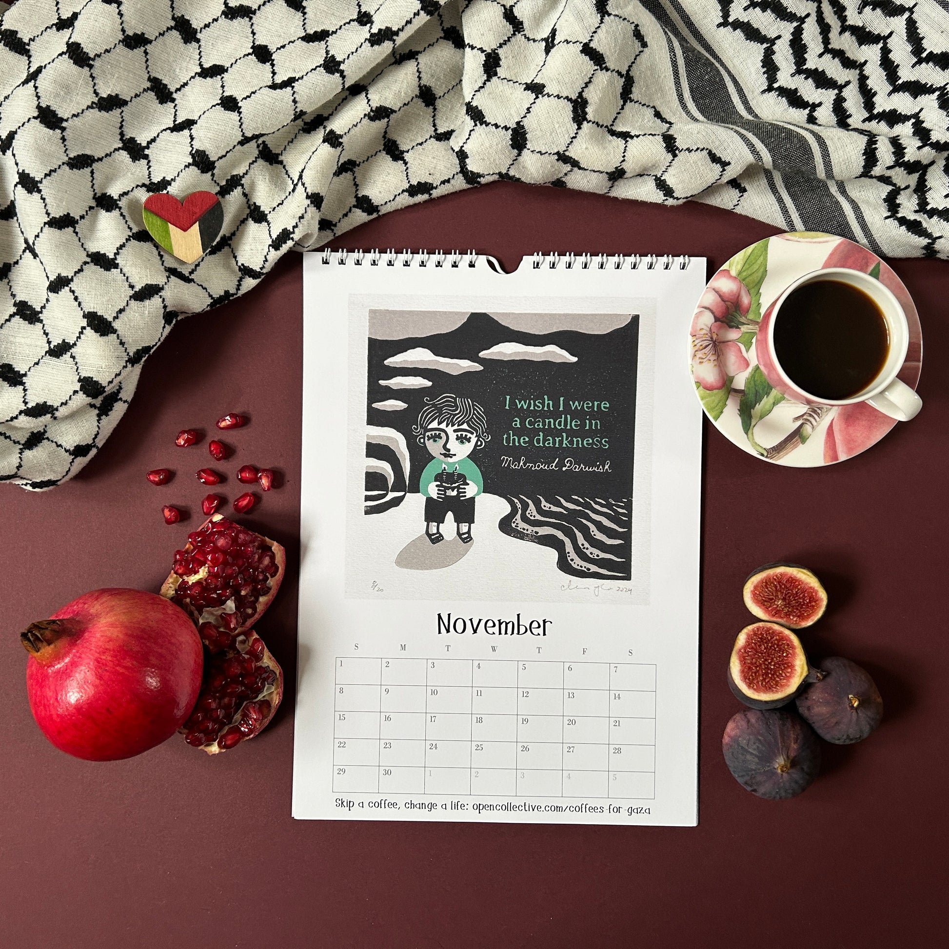 Calendar for November featuring a child holding a candle and quote by Mahmoud Darwish, placed on a surface with fruits and a cup of coffee.